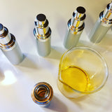 Bottles of face oil and glass beaker with oil blend being filled.
